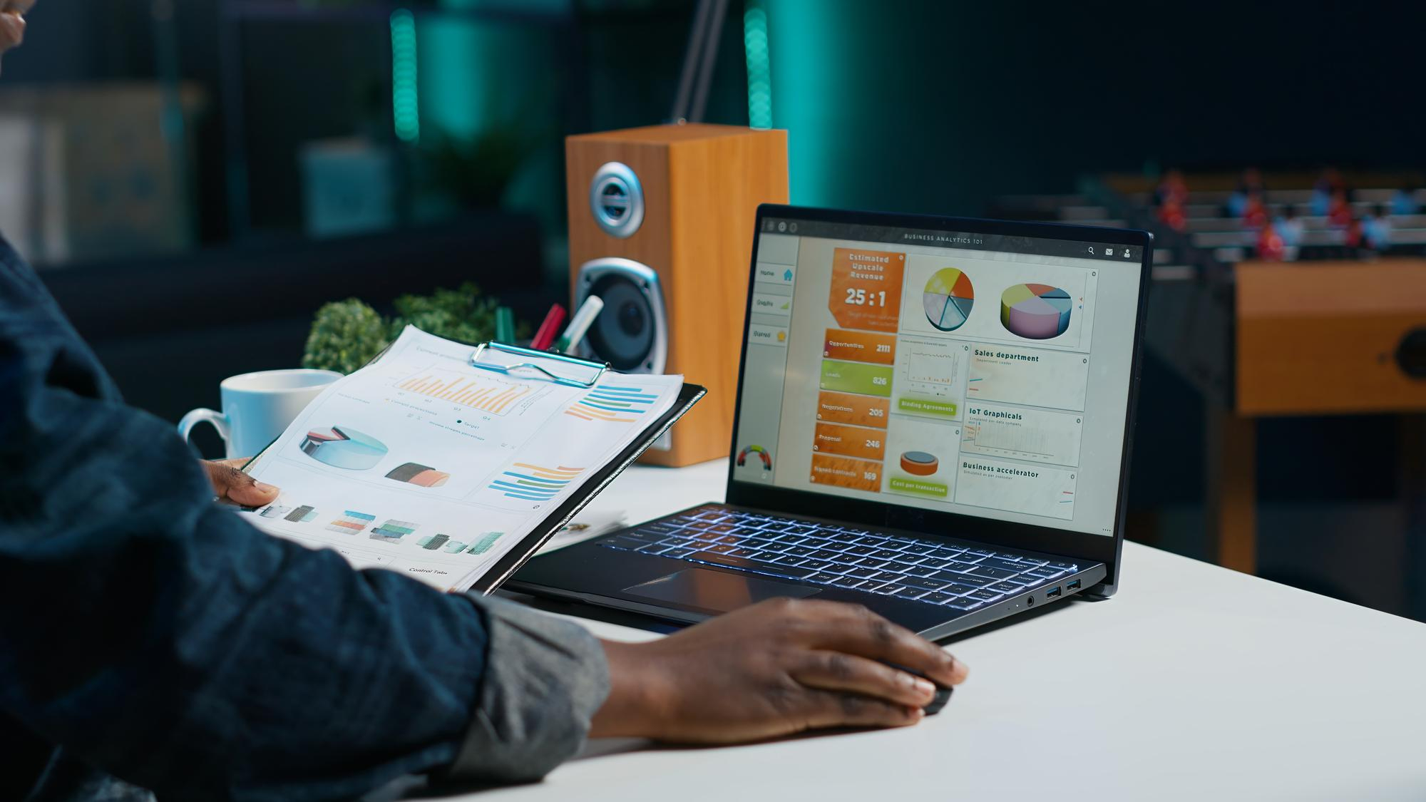 Analyst comparing marketing analytics charts on a laptop and printed report