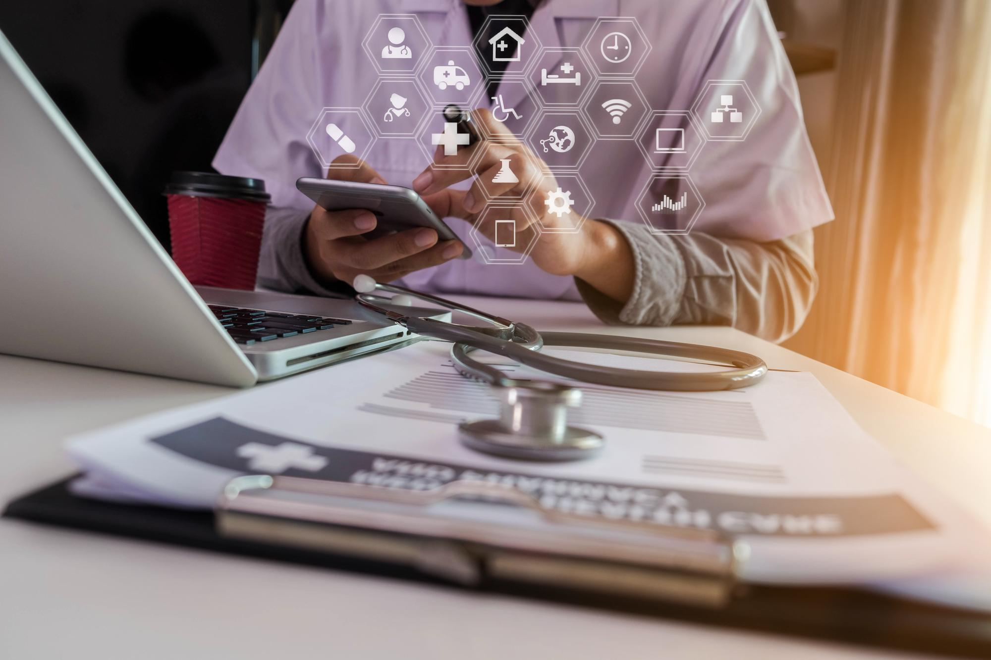 Doctor using a tablet with healthcare icons, stethoscope on the desk