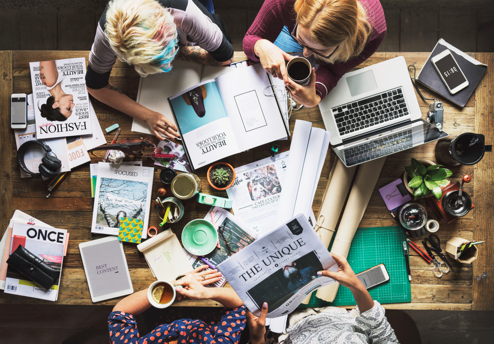 Creative team laying out ad concepts, magazines and laptops on a table
