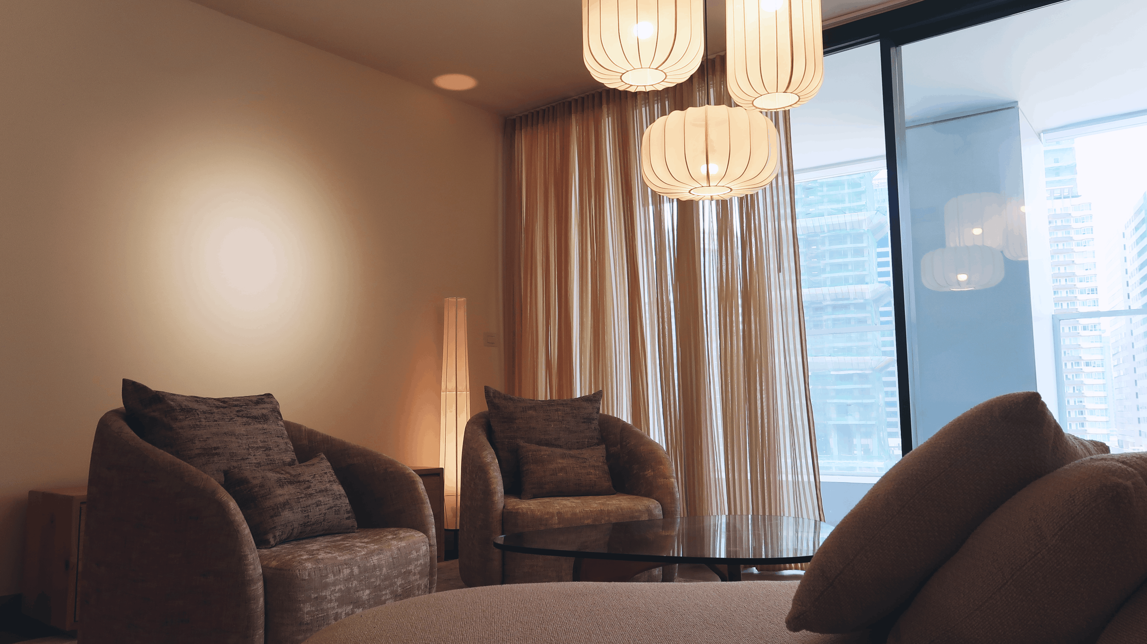 Cozy living room with two armchairs, round glass coffee table, and hanging lantern lights near window. T.M. Kawpeng