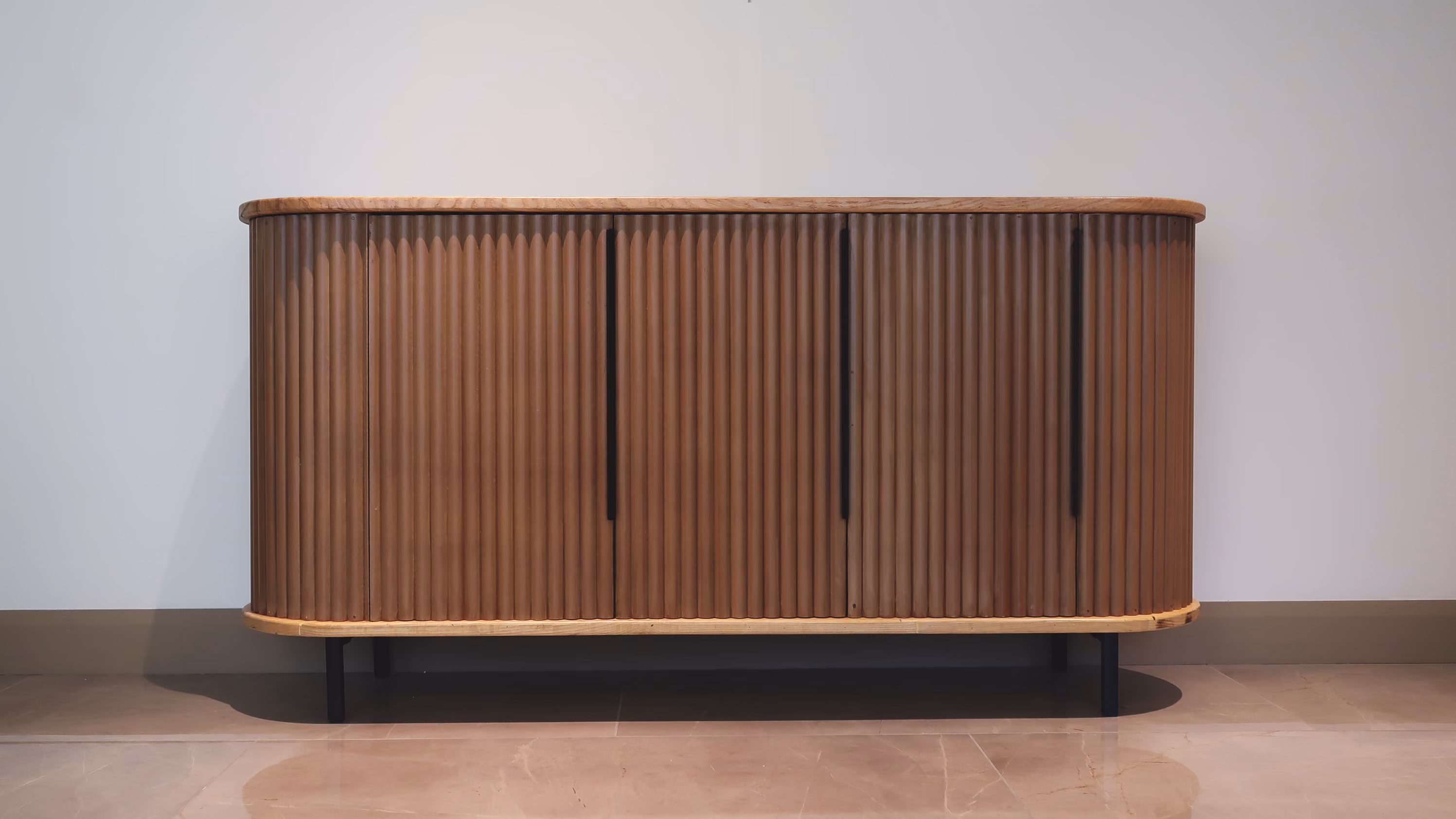 Modern wooden sideboard with vertical slats and black handles on black legs against a light wall. T.M. Kawpeng