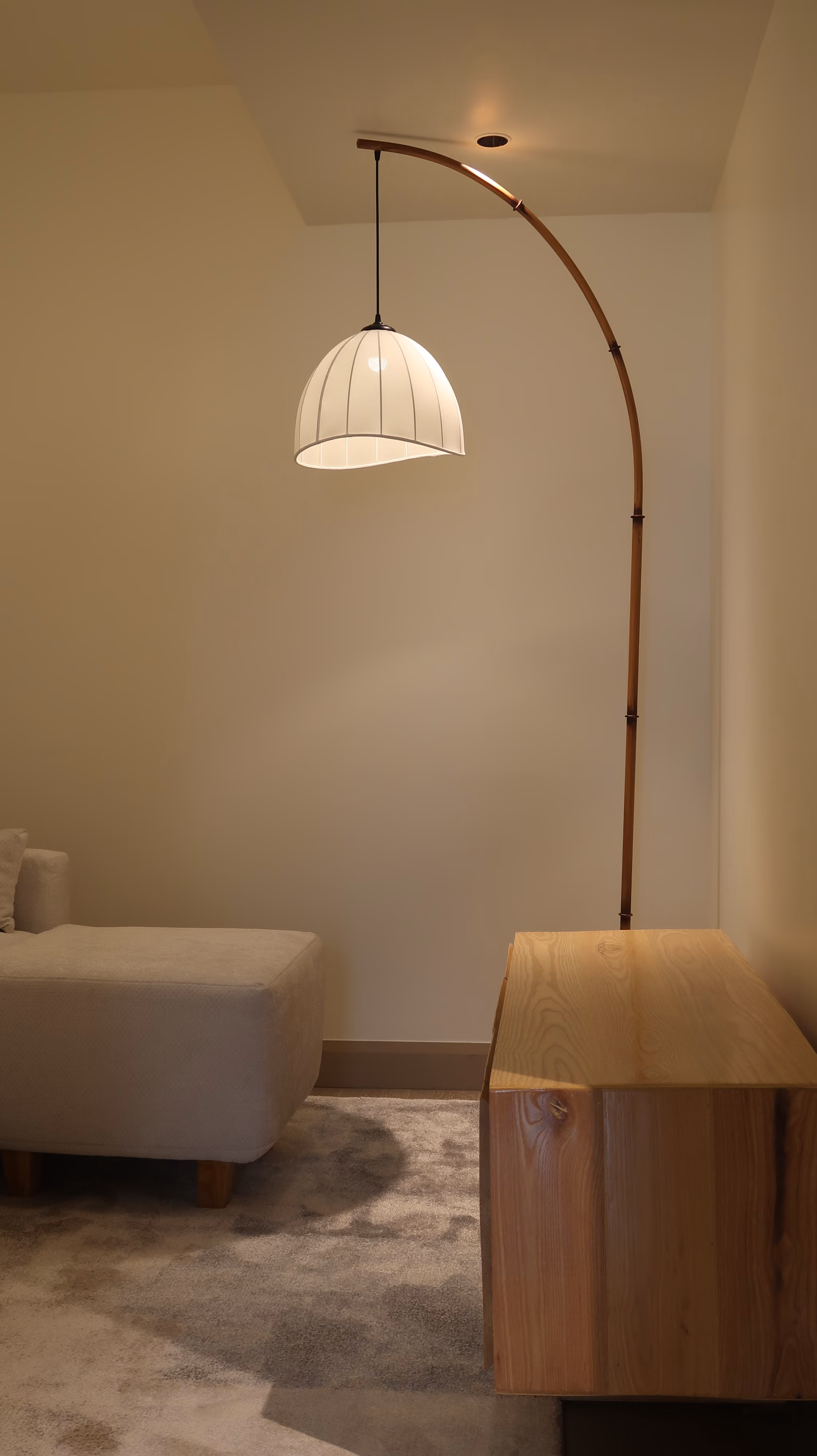 Modern lounge with white curved floor lamp, beige sofa, wooden cabinet, and gray carpet. T.M. Kawpeng