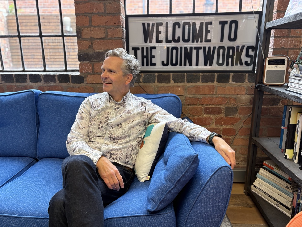 Anthony Tattum on a blue sofa beneath the Welcome to the Jointworks sign
