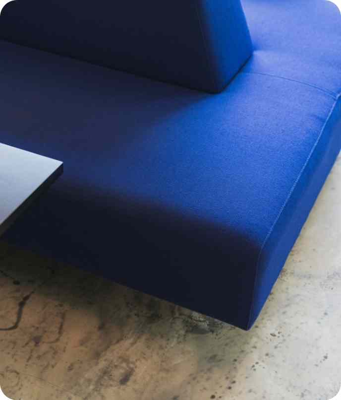 Close-up of a modern blue upholstered sofa corner on a polished concrete floor.