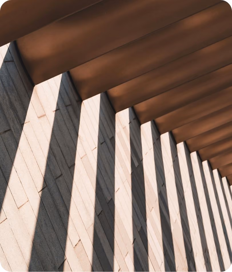 Angular wooden beams casting shadows on a brick wall, creating a pattern of alternating light and shadow.