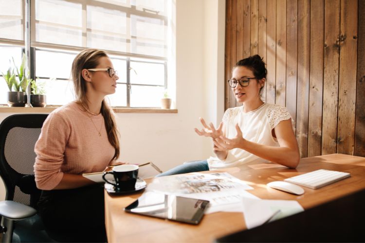 Two women chatting in an office discussing the difference between assignment and sublease
