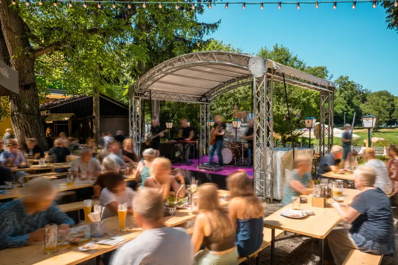 Livemusik auf der Bühne im Biergarten Uferstüble, Gäste an Biertischen