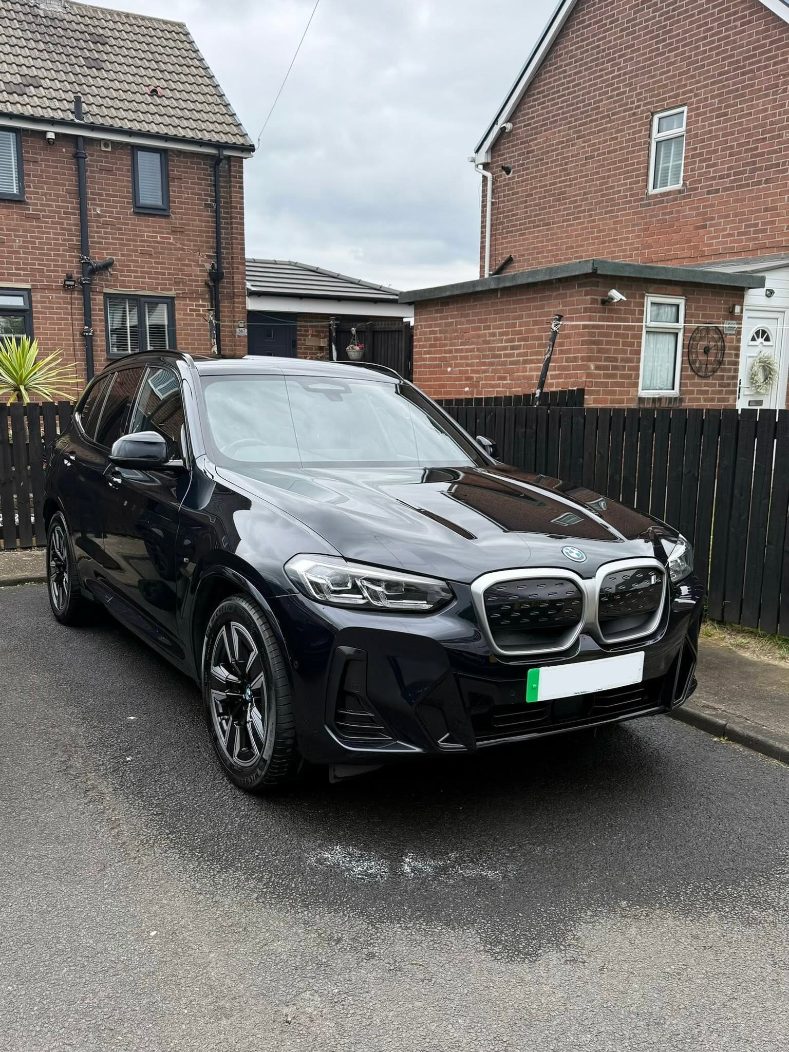Black BMW SUV parked on a residential street near brick houses and black wooden fences.