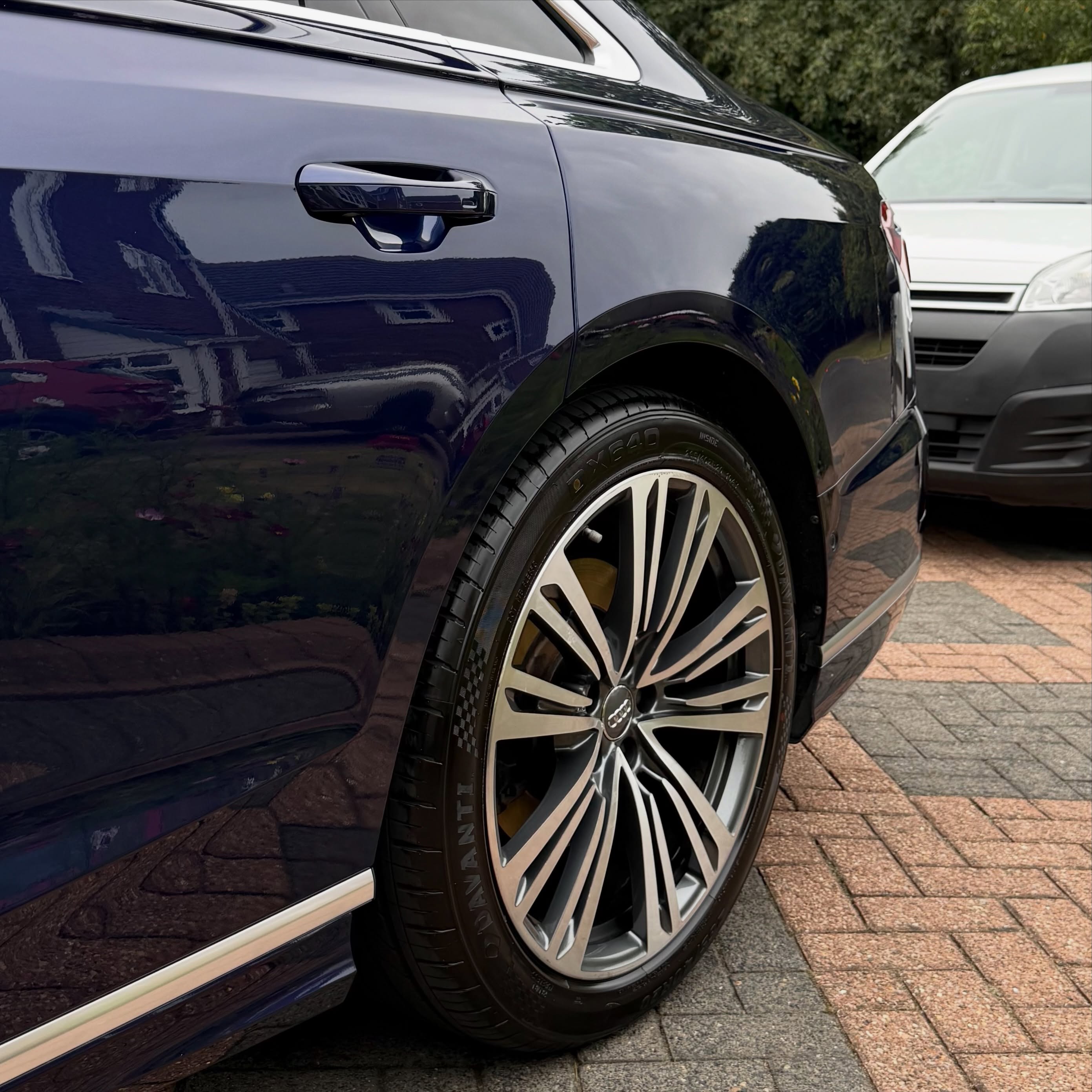 Close-up of a dark blue car's rear wheel and door with a silver-striped alloy rim parked on a brick driveway.
