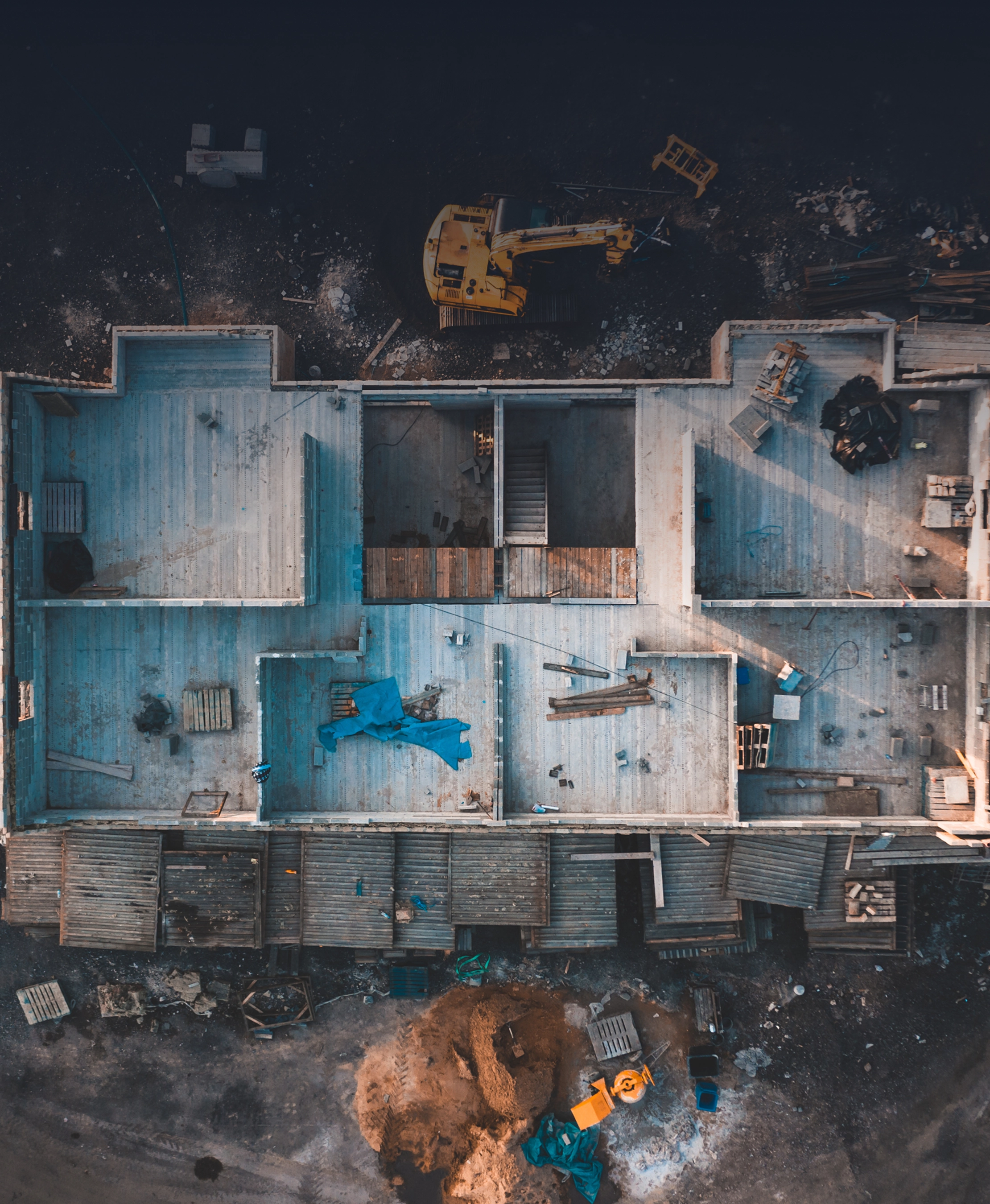 Aerial view of a construction site with building foundations, an excavator, and construction materials.