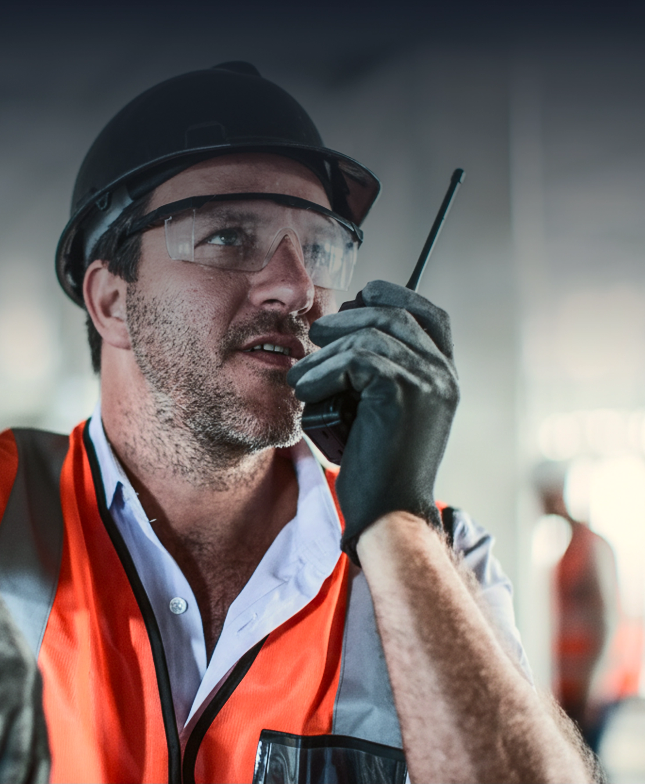 Construction worker wearing safety gear speaking into a walkie-talkie on site.