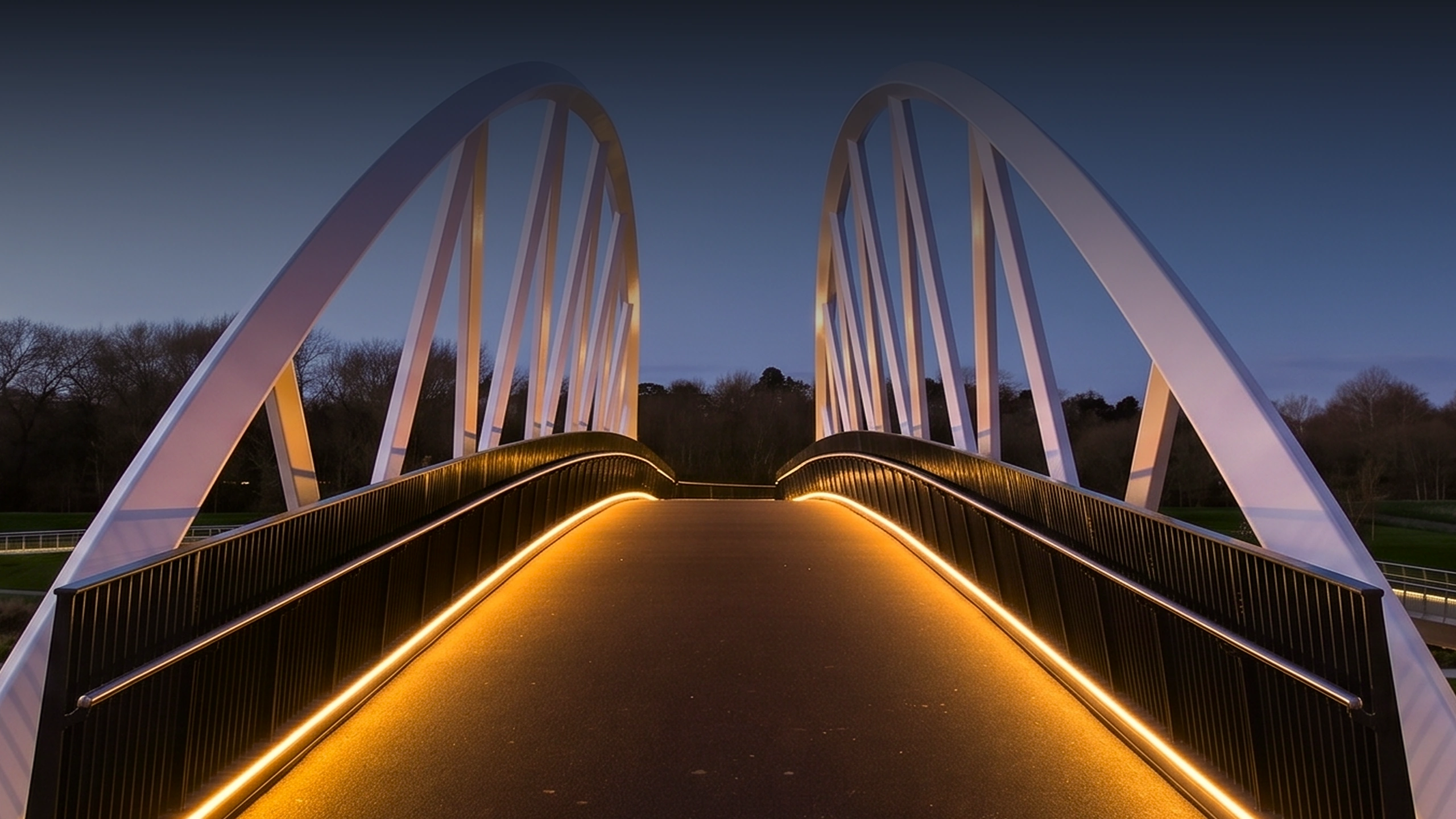 Modern pedestrian bridge with white arches and orange LED lights along the sides at dusk.
