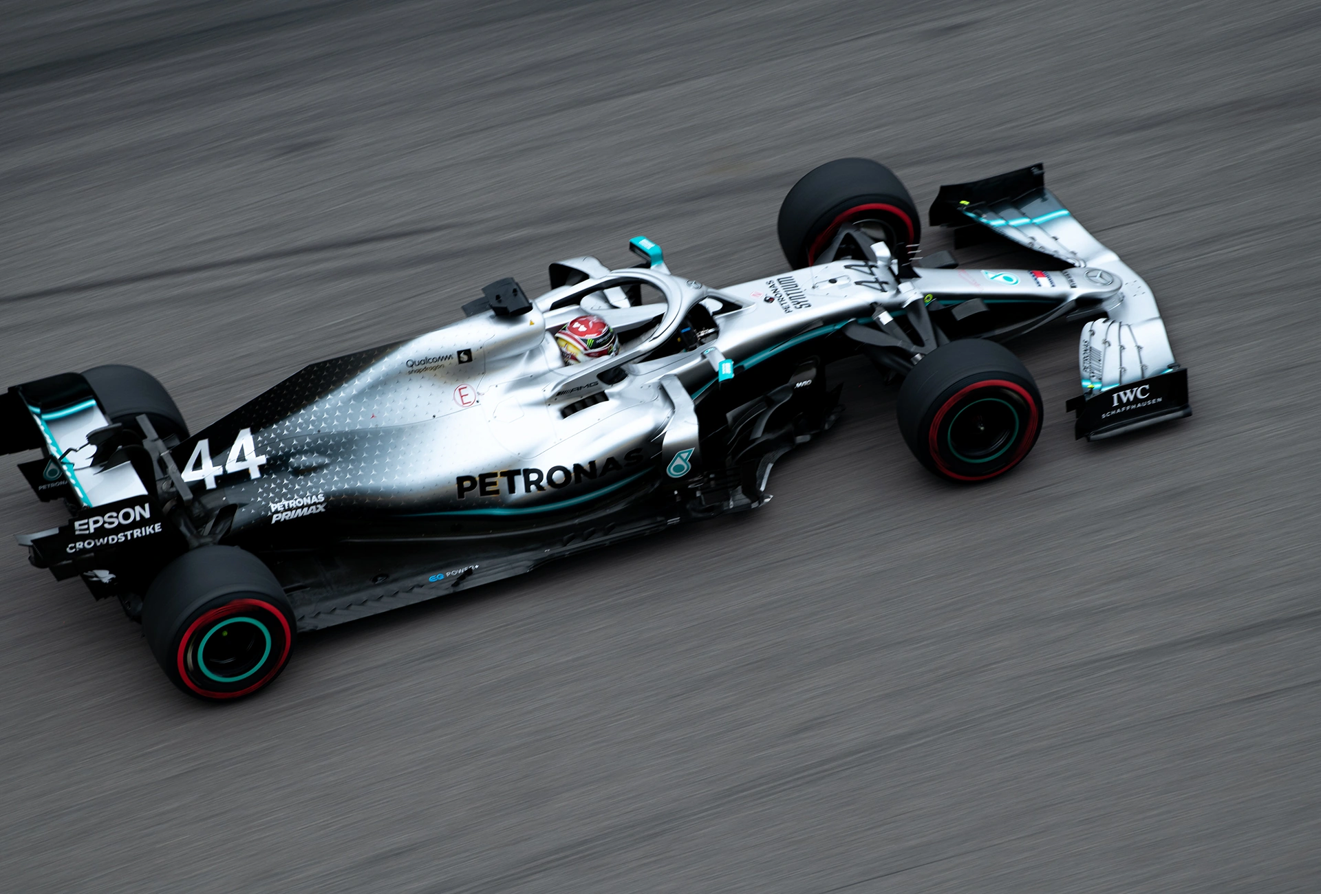 Silver Formula 1 race car with number 44 racing on a track with blurred asphalt surface.