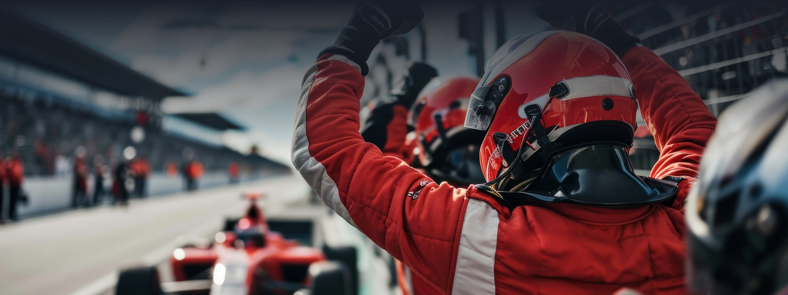 Race car team in red suits and helmets celebrating as car enters pit lane during race.