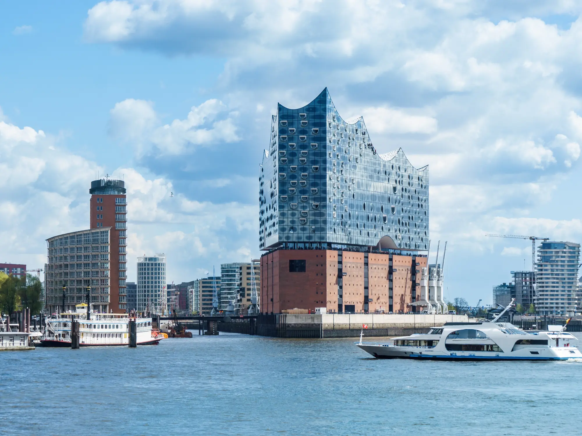 Elbphilharmonie concert hall in Hamburg with water and boats on a partly cloudy day.