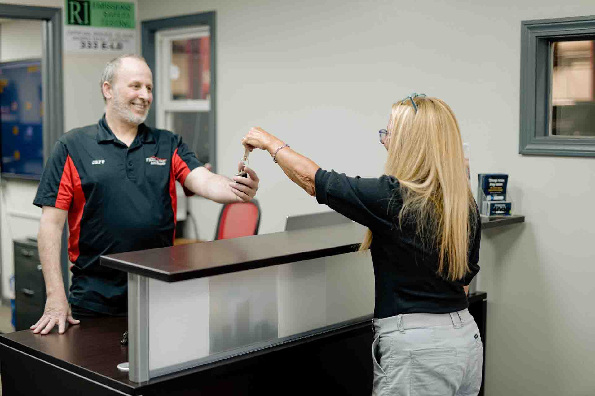 Primary Care Auto Repair service advisor handing car keys to a smiling customer after completing their vehicle service.