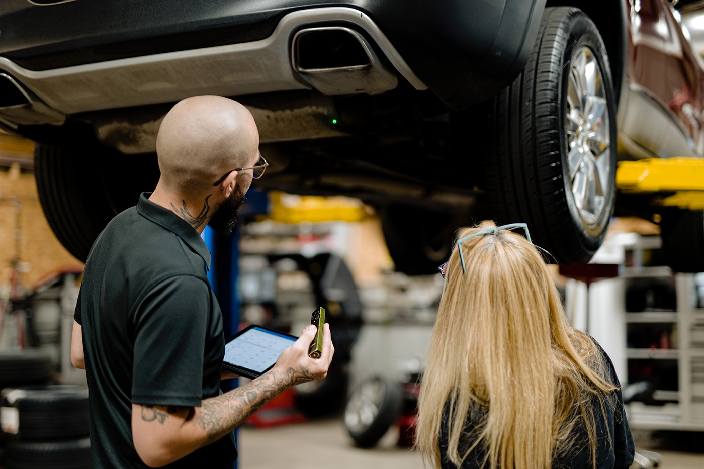 Primary Care Auto Repair service advisor reviewing a vehicle inspection with a customer using a digital tablet in the service bay.