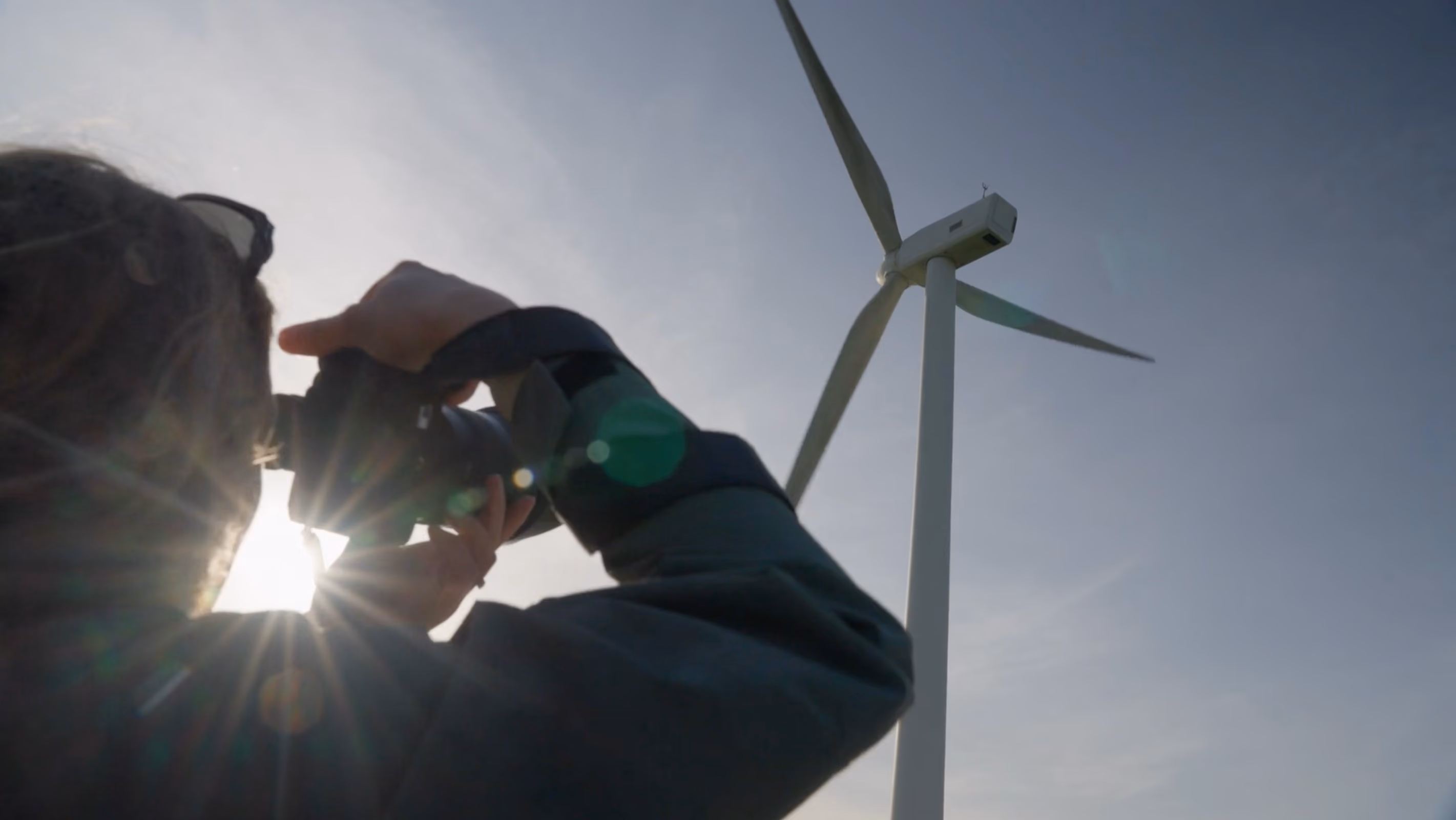 Person looking through binoculars towards a wind turbine in the Wildtribe brand film