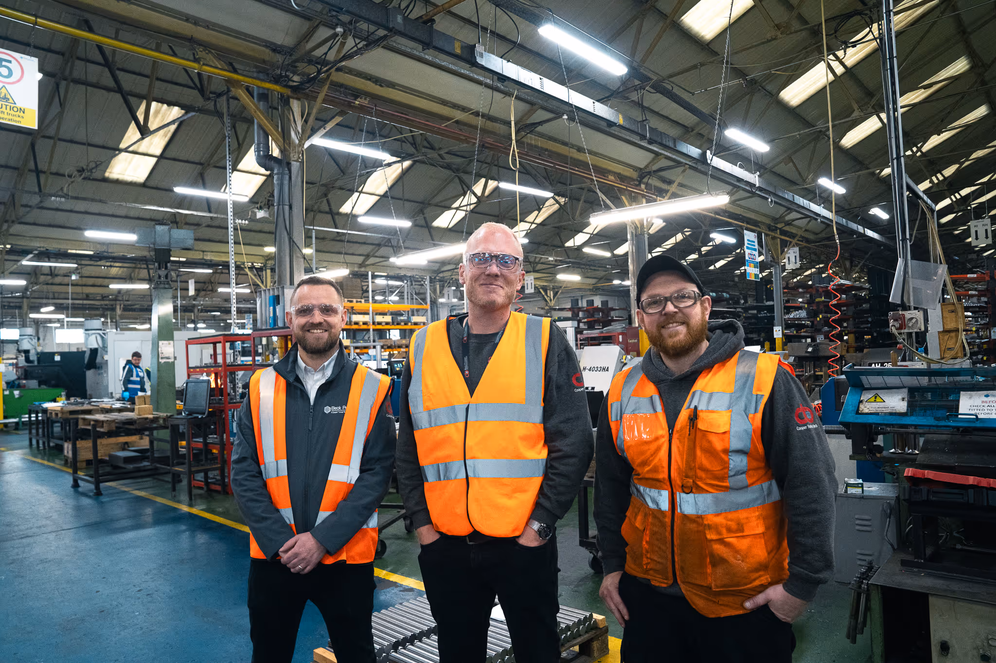 Three colleagues wearing high visibility vests on a factory floor