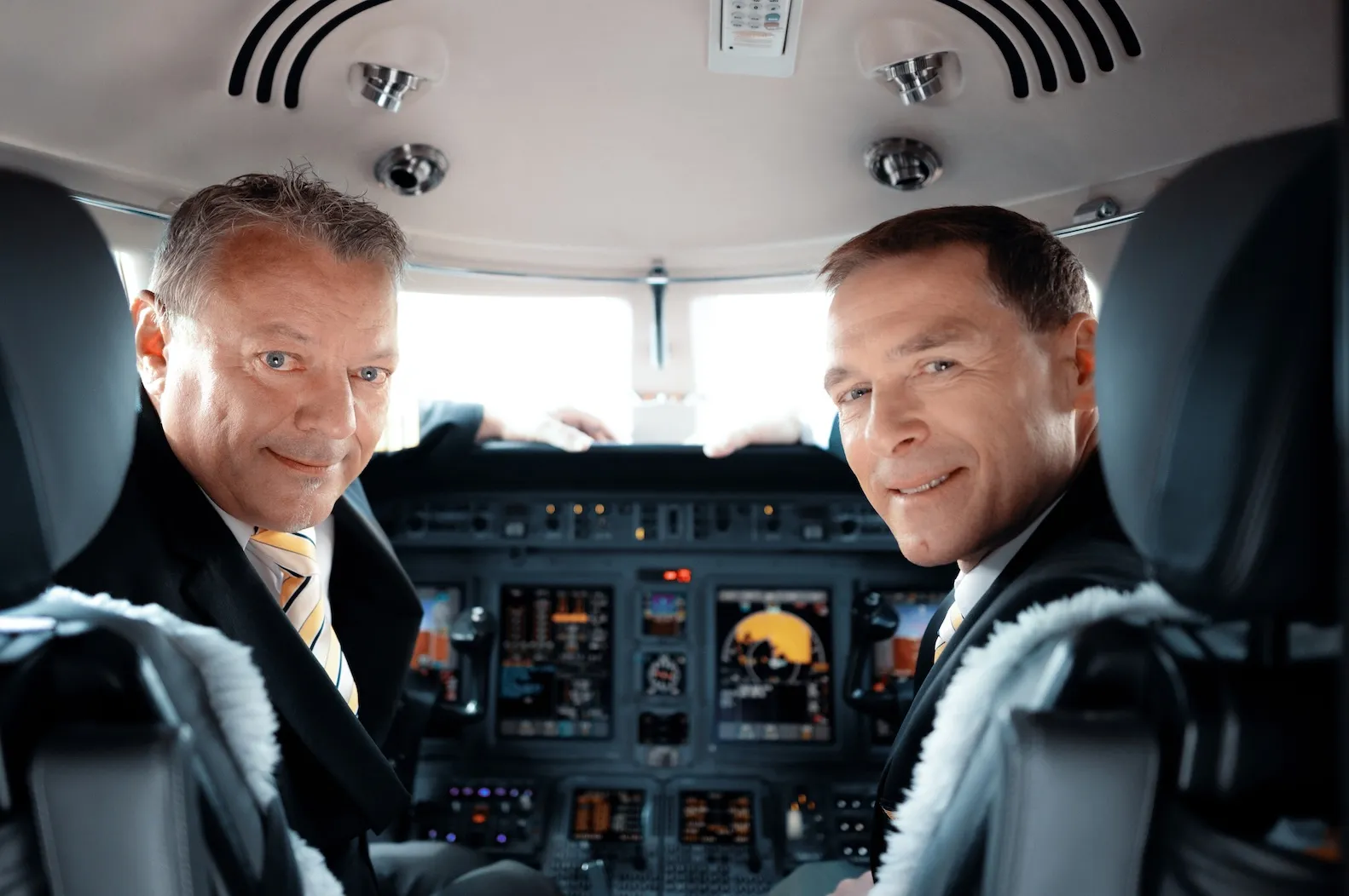 Dva piloté Air Bohemia v kokpitu se otočili a usmívají se