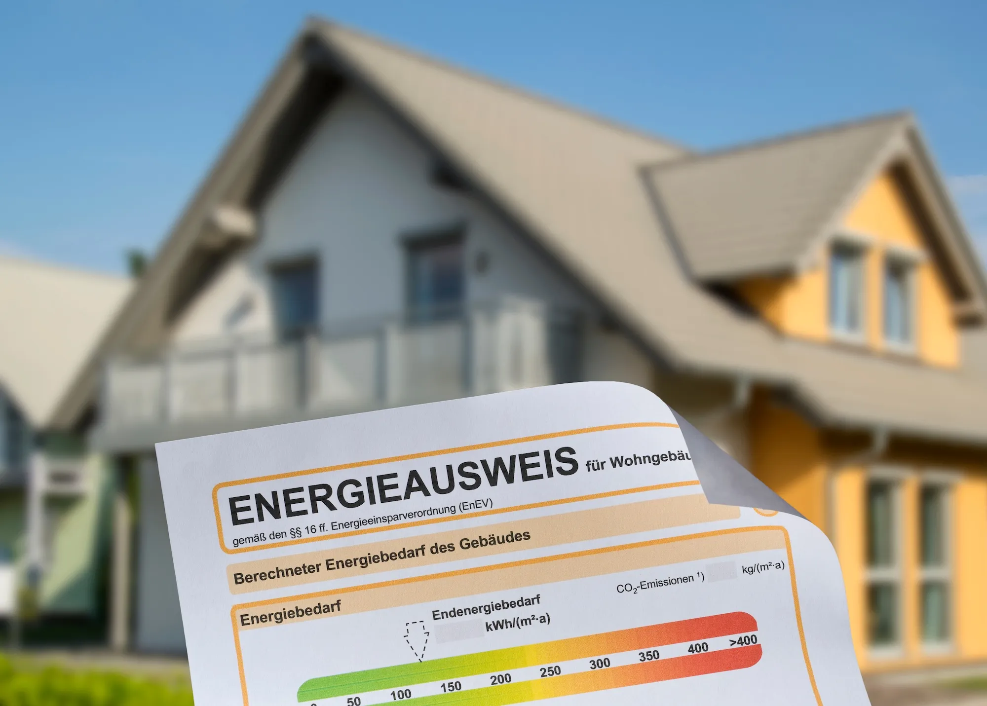 Ein Energieausweis zeigt berechneten Energiebedarf vor einem Wohnhaus.