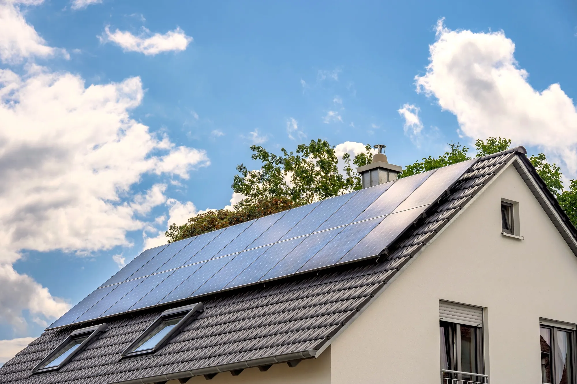 Haus mit Solarpanelen auf dem Dach unter blauem Himmel mit Wolken.