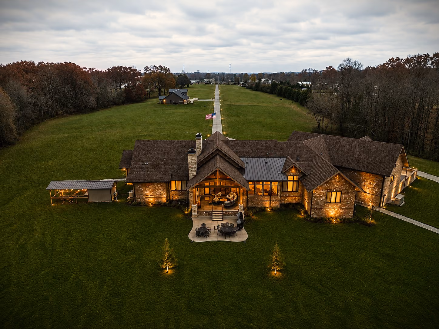 Aerial view of a Hannah Custom Homes estate lit up at dusk with a long tree-lined driveway.