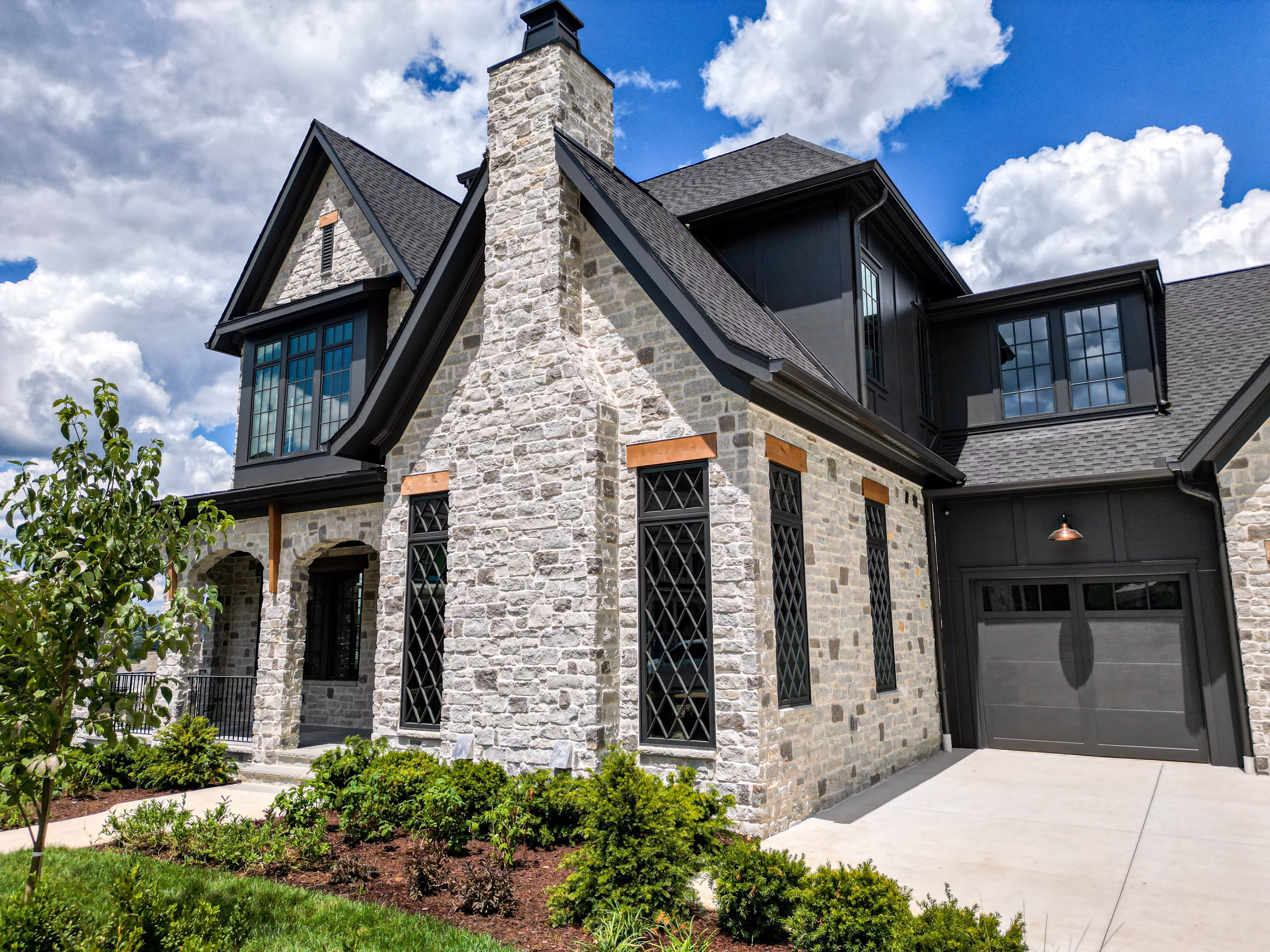 Close-up of a stone-facade home built by Zurich Homes, with a steep gabled roof and dark garage door.