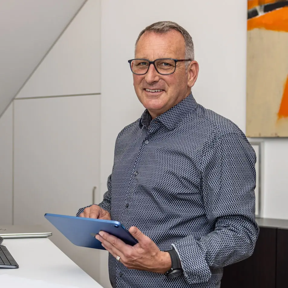 Lächelnder Mann mit Brille hält ein Tablet im modernen Büro.