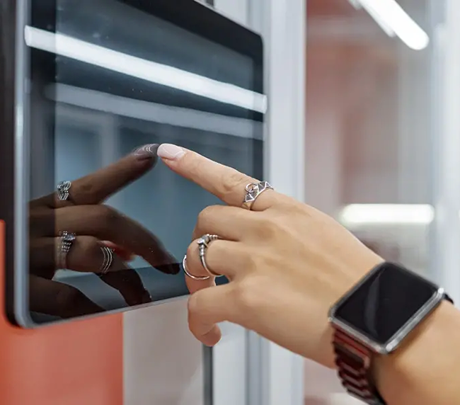 Hand mit Ringen und Smartwatch bedient Touchscreen an der Wand.