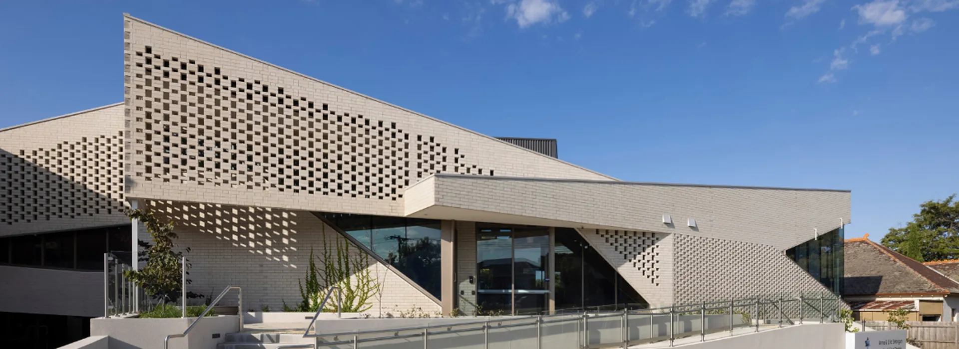 Modern building with beige brick walls featuring geometric cut-out patterns and glass entrance.