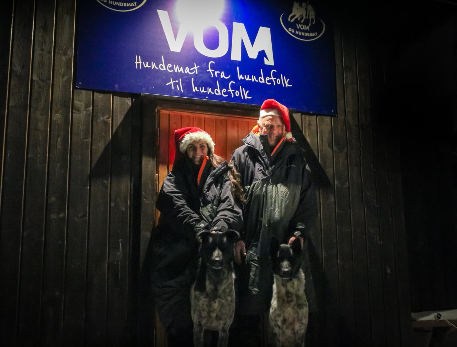 Under the Vom og Hundemat sign at the kennel, with two of the dogs