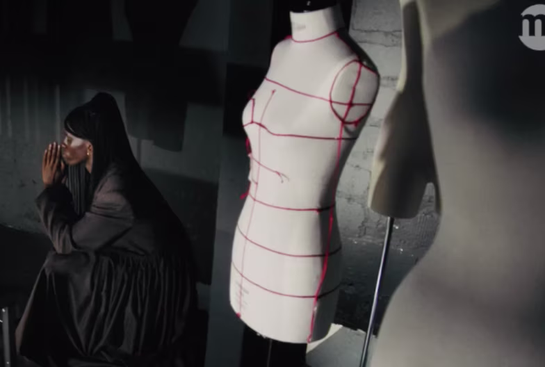 Person in dark clothing sits next to two white dressmaker mannequins with red measuring lines.