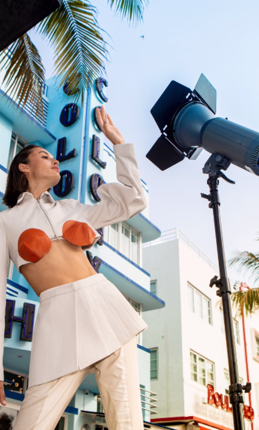 Woman in stylish white outfit posing outdoors by palm trees and a blue Art Deco building.