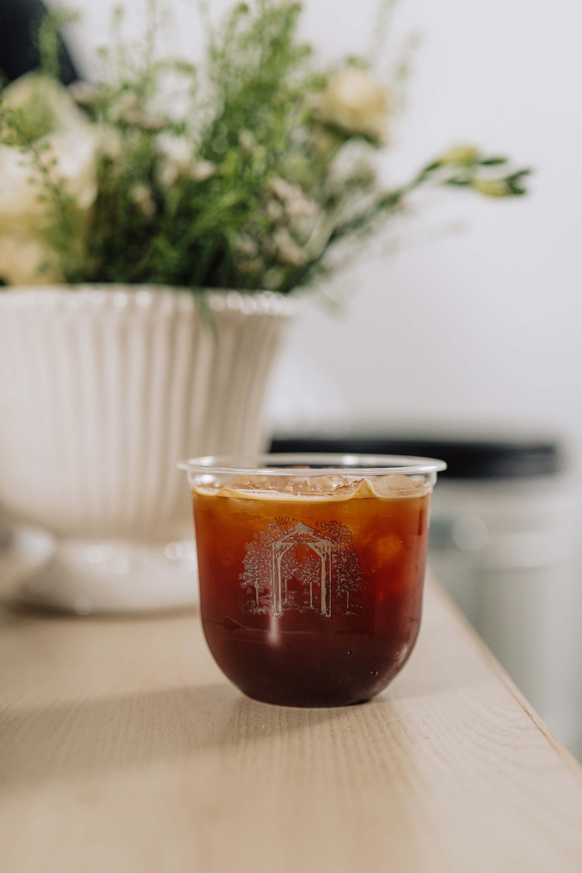 White pedestal vase of flowers beside an iced coffee