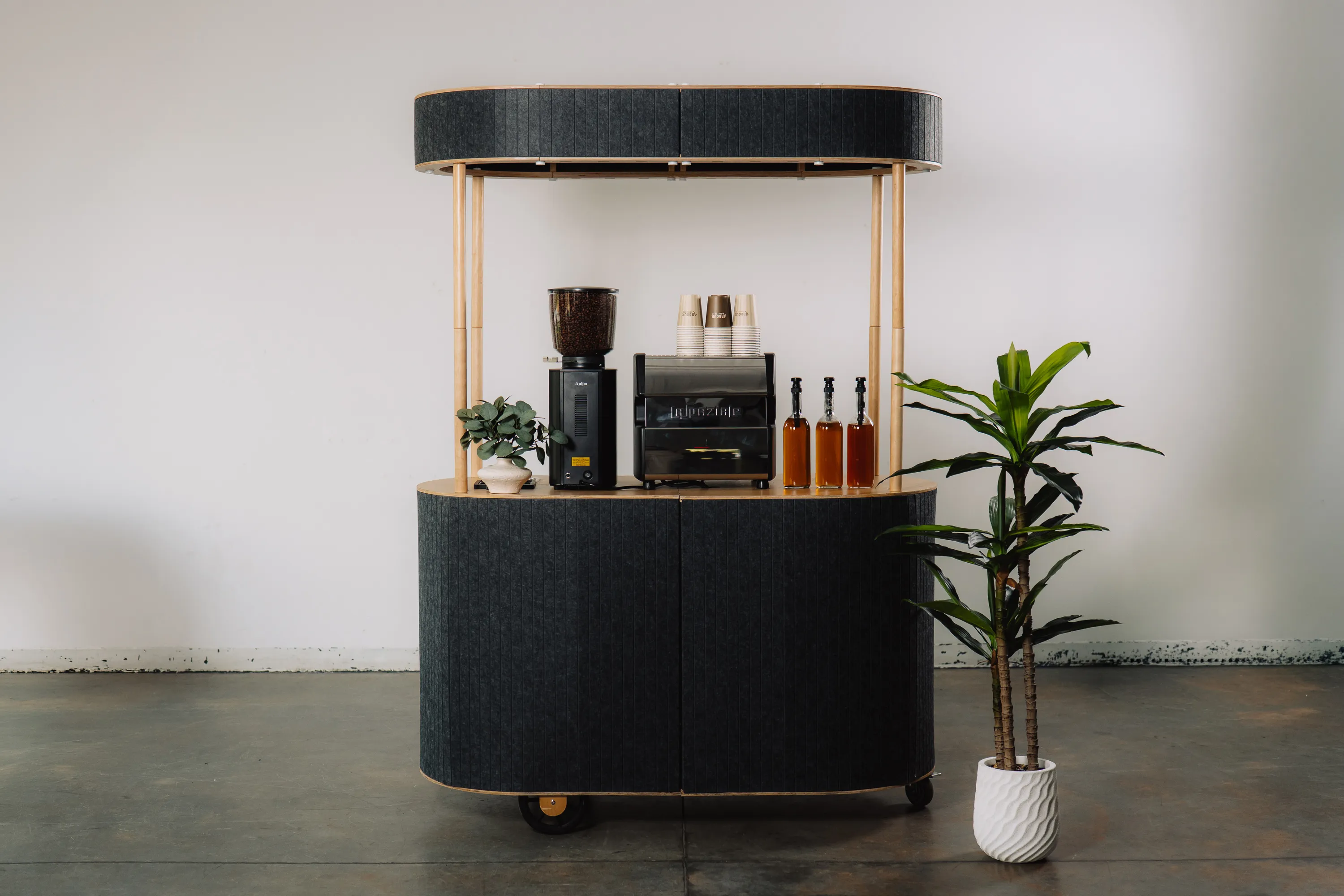 Modern mobile espresso bar cart with espresso machine and grinder next to a potted green plant.