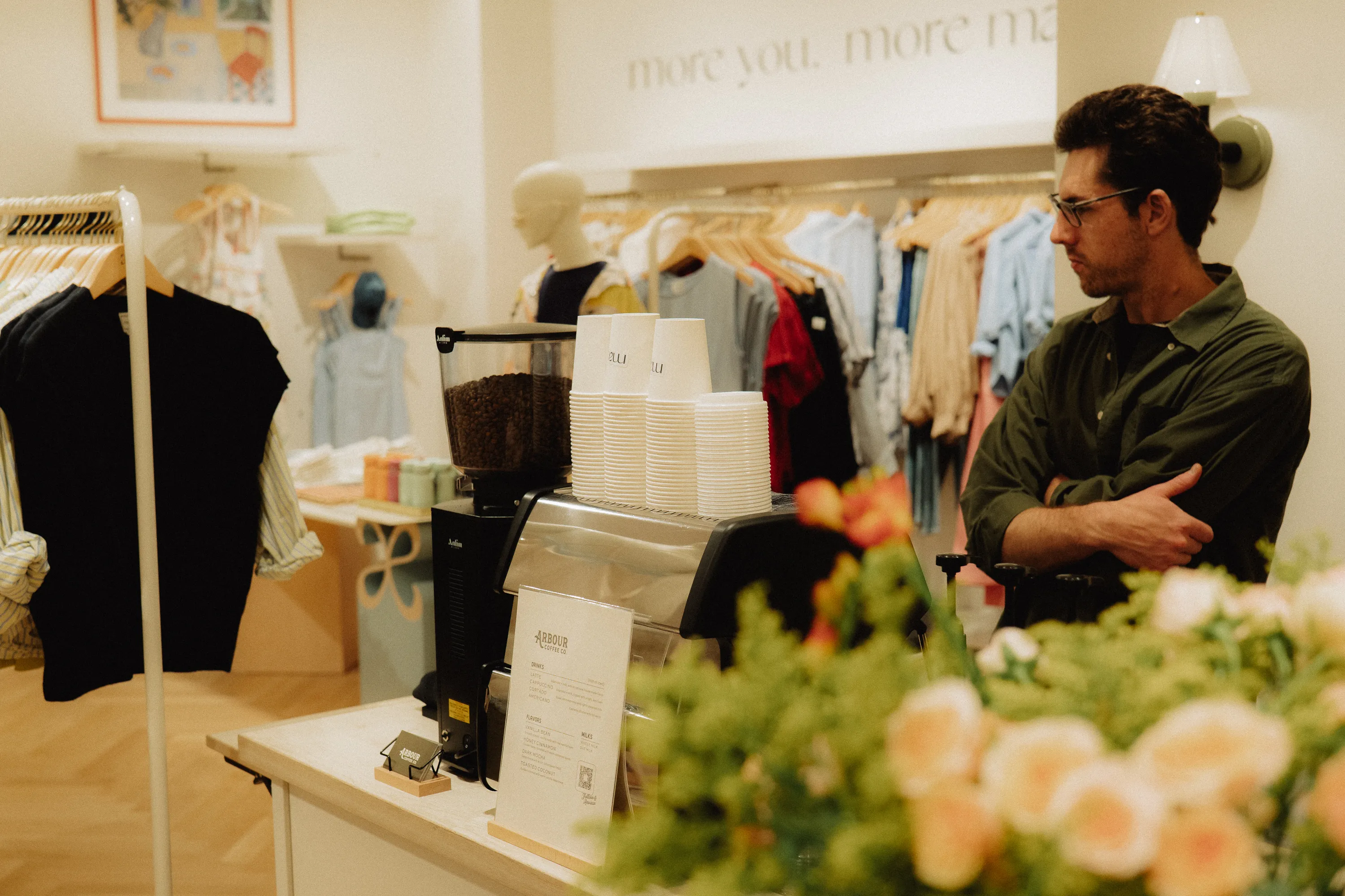 A barista stands behind a mobile Arbour Coffee Co. espresso bar setup inside a brightly lit clothing boutique.