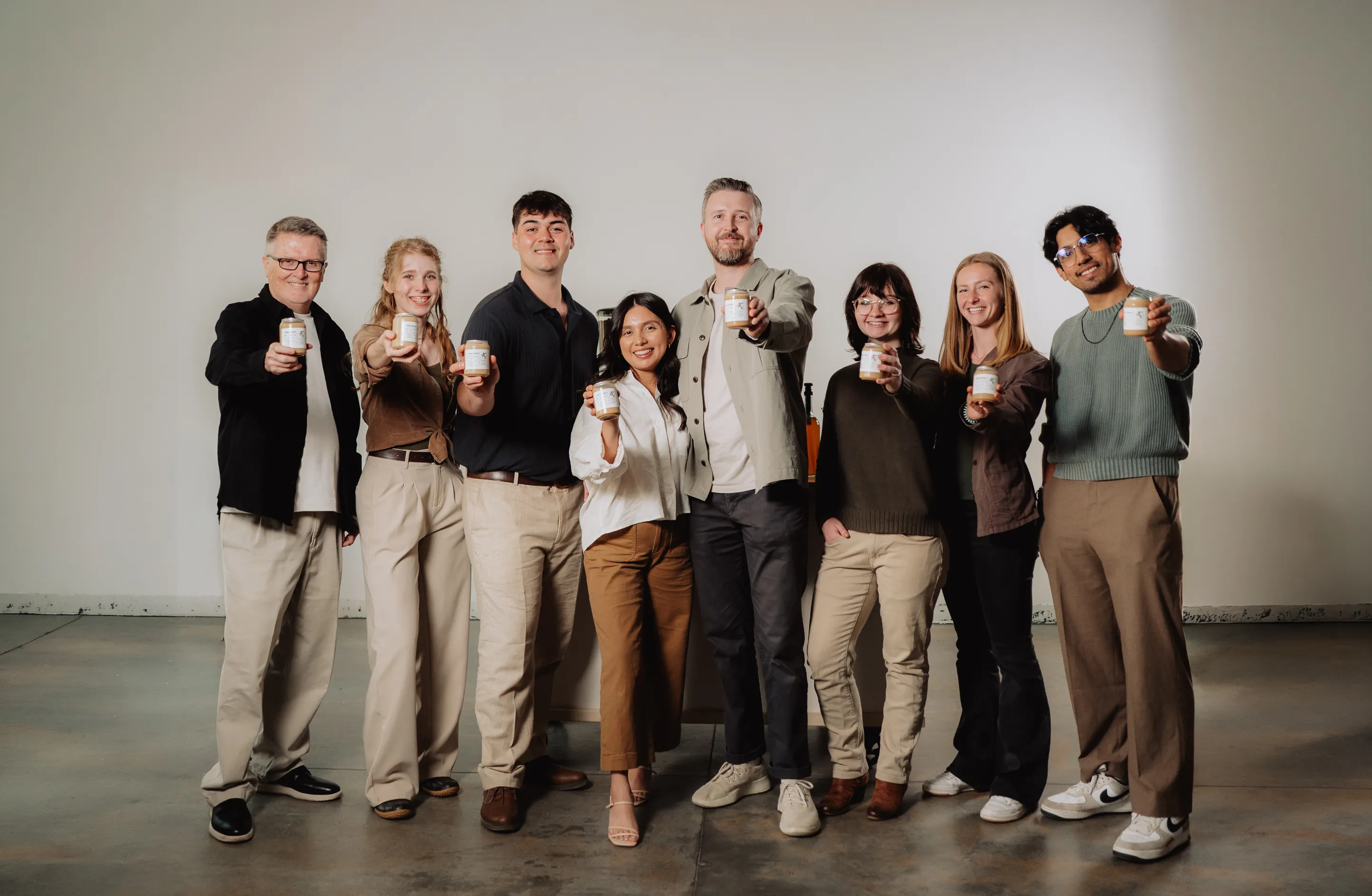 A group of eight smiling people in a studio posing together and holding up small jars of product.