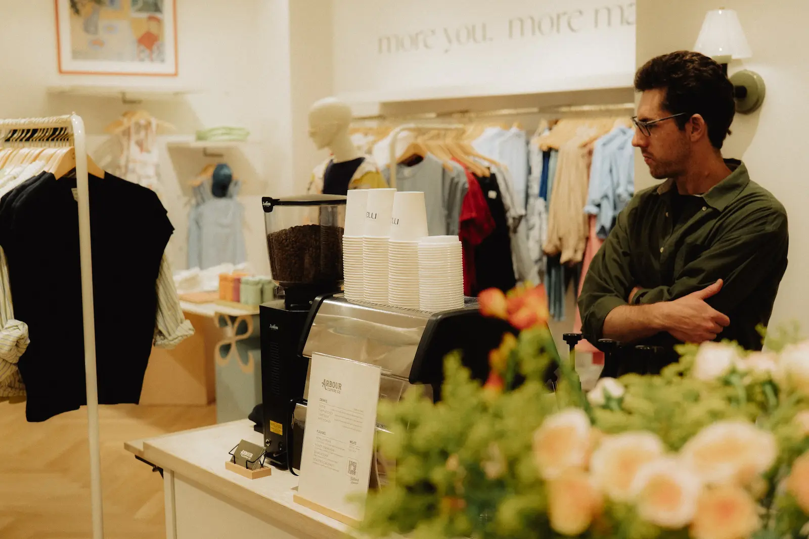 A barista stands behind a mobile Arbour Coffee Co. espresso bar setup inside a brightly lit clothing boutique.