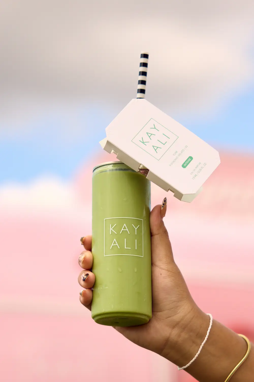A guest holding a green Kayali-branded canned drink with a scent card on the straw