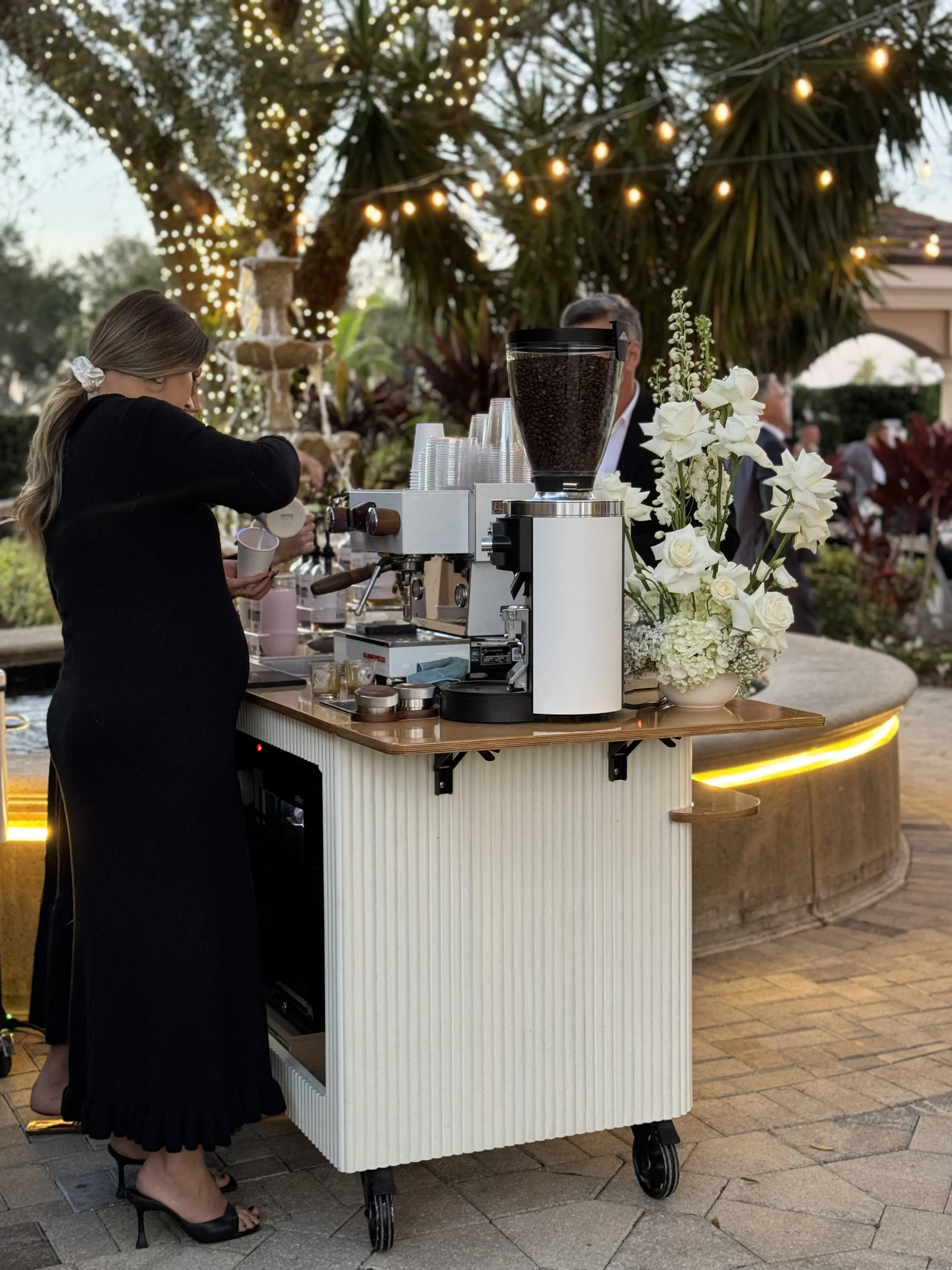 Barista serving from the Storii cart at an evening event under string lights