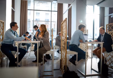 Deux paires de personnes discutent assises à des tables séparées dans un café moderne.
