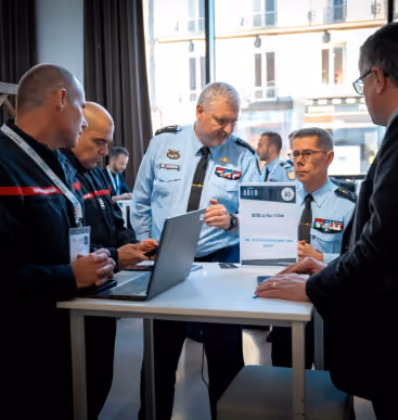 Quatre hommes en uniforme et un homme en costume discutent autour d'une table avec un ordinateur portable.