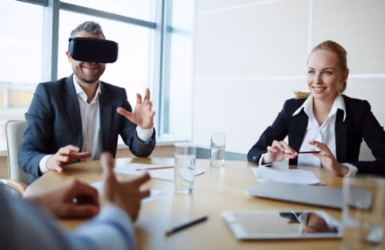 Homme en costume utilisant un casque VR à une table de réunion avec deux collègues souriants.