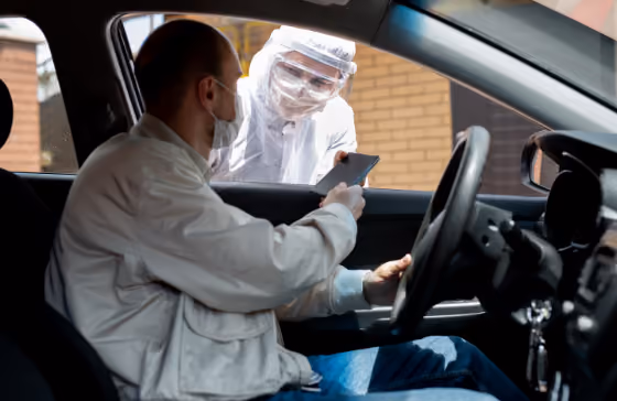 Un conducteur remet son téléphone à une personne en tenue de protection lors d'un test Covid en voiture.
