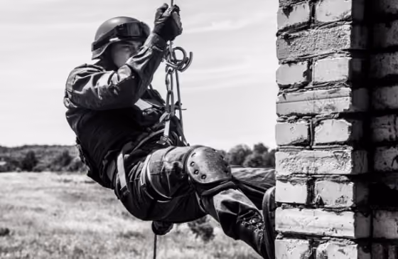 Personne équipée descend en rappel le long d'un mur en briques dans un champ.