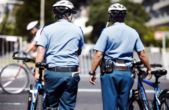 Deux policiers à vélo en uniforme bleu, vus de dos en train de marcher.