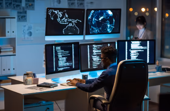 Deux professionnels de la cybersécurité travaillant sur plusieurs écrans avec du code et des données géographiques.