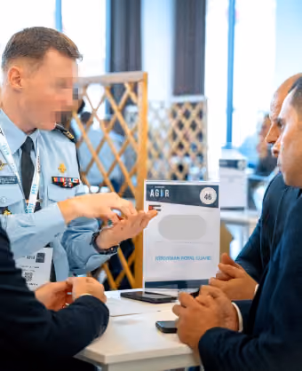Quatre hommes discutent à une table lors d'un événement professionnel en intérieur.