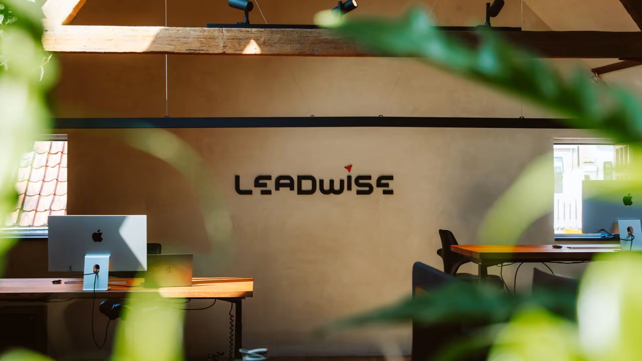 Kantoorruimte met houten balken, bureaus met computers en muur met het woord Leadwise.